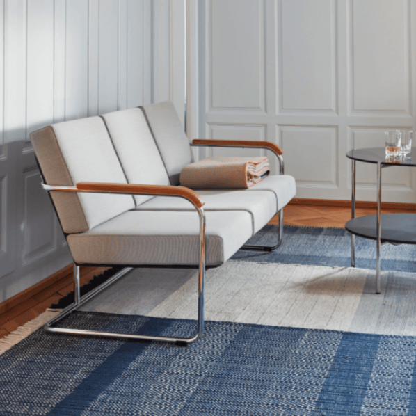 Ein minnimalistisch gehaltenes 3-Sitzer Sofa steht auf einem blauen Teppich